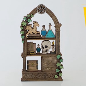 Puede incluir: Estantería de madera con diseño de arco gótico, con un dragón, botellas de pociones, una calavera y un pentagrama. La estantería está decorada con hiedra verde y un cofre del tesoro. El diseño es en tonos marrones y beige.