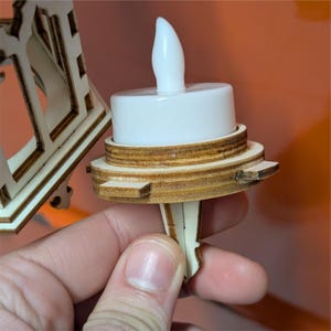 May include: A close-up of a white LED candle with a wooden base. The candle has a realistic flame shape and is part of a wooden decorative piece. The wooden base is intricately designed with multiple layers and details.