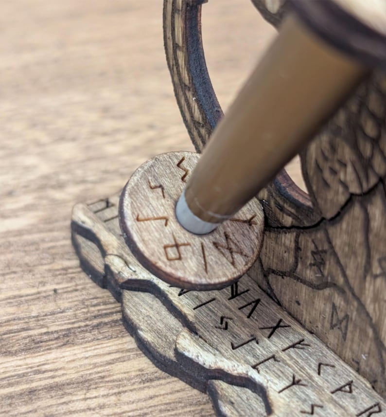May include: Close-up of a wooden desk accessory with engraved runes. The accessory features a circular piece with runes and a brown pen holder. The wood has a natural grain and a warm, brown tone. The design appears to be laser-cut.
