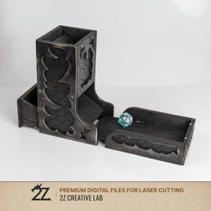 May include: A black wooden dice tower with a distressed finish and intricate dragon scale cutouts on the sides. The tower features an attached tray at the base containing a single teal twenty-sided die. The text 2Z CREATIVE LAB is visible.