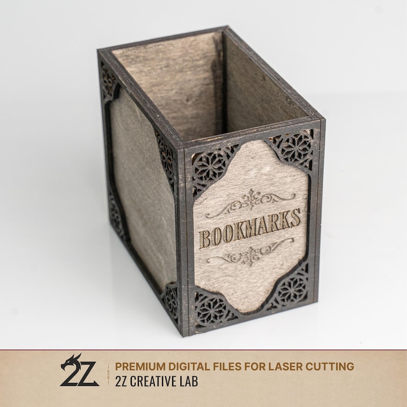 May include: A wooden bookmark holder with a rectangular shape and a light brown interior. The exterior is dark brown with decorative cut-out patterns and the word "BOOKMARKS" engraved on the front.