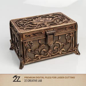 Può includere: Una scatola rettangolare con finitura bronzo scuro caratterizzata da intricati motivi floreali e di viti tagliati al laser sul coperchio e sul pannello frontale. La scatola ha una chiusura centrale e poggia su quattro piedini decorativi. Testo 2Z CREATIVE LAB.