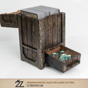 Könnte beinhalten: Eine Holzbox zur Aufbewahrung von Karten und Würfeln mit rustikalem, verwittertem Aussehen. Die Box hat eine Schublade mit grünen Würfeln und ein Fach mit einem Stapel Karten. Das Design umfasst gravierte Details und einen Klappdeckel.
