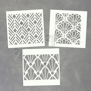 May include: Three white stencils with Art Deco designs. One stencil features a geometric pattern of chevrons, another has a fan-like design, and the third has a diamond and triangle pattern. The stencils are square and have the text "2 CREATIVE LAB".