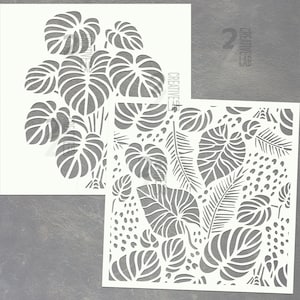 Può includere: Due stencil bianchi con disegni di foglie tropicali. Uno stencil mostra una grande pianta di monstera, mentre l'altro mostra una varietà di foglie e motivi a pois. La parola "CREATIVE" è stampata sul lato degli stencil. Il numero 2 è anche visibile.