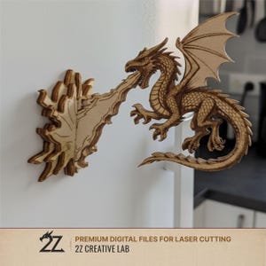Op de afbeelding: Een houten drakenfiguur met gedetailleerde schubben en vleugels, die vuur spuwt naar een aparte vlam. De afbeelding bevat de tekst "PREMIUM DIGITAL FILES FOR LASER CUTTING" en "2Z CREATIVE LAB".