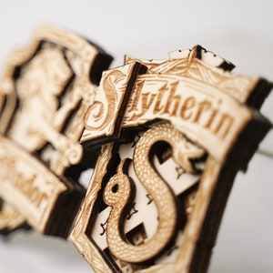 Könnte beinhalten: Zwei Holzschilde der Harry-Potter-Häuser, eines für Slytherin mit einer Schlange und das andere für Hufflepuff mit einem Dachs.