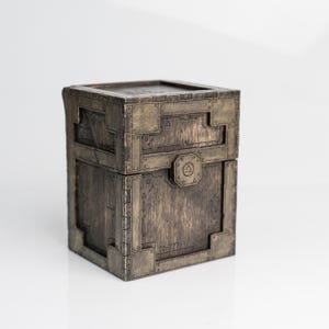 May include: A wooden box with a metallic, industrial design. The box is square with a hinged lid and features metal plates, rivets, and a circular emblem. The color is a mix of brown and bronze, giving it a vintage look.