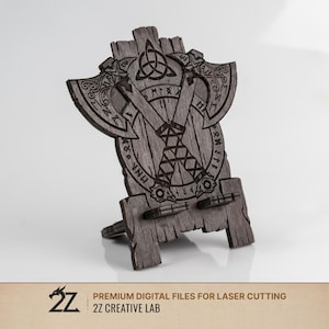 Puede incluir: Un soporte decorativo de madera gris con un diseño de hacha vikinga. El soporte tiene intrincadas tallas, incluyendo runas y un nudo celta. La base es ajustable y el diseño es adecuado para corte por láser.
