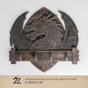 Op de afbeelding: Houten wanddecoratie met een gedetailleerd drakenontwerp. De draak is gesneden met uitgespreide vleugels en een felle uitdrukking, tegen een schildvormige achtergrond. Daaronder een houten balk met drie haken. Het stuk is afgewerkt in bruin- en grijstinten.