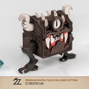 May include: A dark brown wooden chest creature with a single large eye, sharp white teeth, and curved horns. The box features red accents inside the mouth and dark legs. Text at the bottom reads: 2Z PREMIUM DIGITAL FILES FOR LASER CUTTING 2Z CREATIVE LAB.