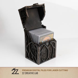 Może przedstawiać: Ciemnobrązowe drewniane pudełko na karty z otwartą pokrywą na zawiasach, ozdobione na zewnątrz misternymi, wyciętymi laserowo wzorami korzeni lub gałęzi. Pudełko zawiera stos kart do gry z widocznym napisem Magic na wierzchniej karcie.