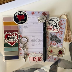 May include: A selection of thriller-themed accessories, including stickers, a bookmark, a pen, and a keychain. The stickers display phrases such as "Thriller Reader" and "The Plot Thickens." The bookmark has a tassel and the text "Sink My Teeth Into."