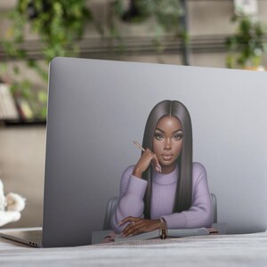 May include: A laptop computer with a sticker of a woman with long black hair wearing a purple sweater and looking thoughtfully at a pencil. The woman is sitting at a desk with a notebook in front of her.