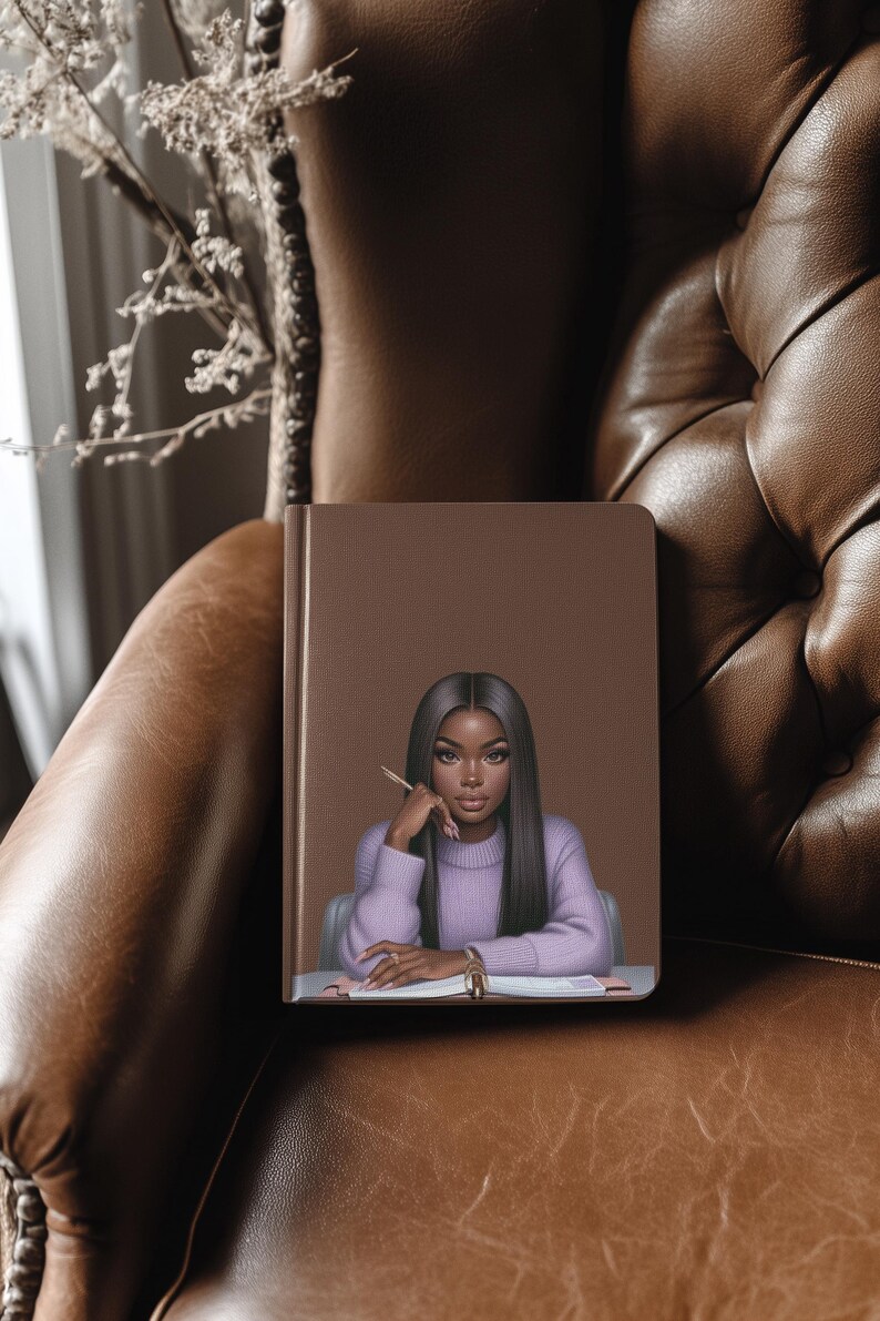 May include: A brown leather-bound journal with a colorful illustration of a woman with long black hair, wearing a purple sweater, sitting at a desk with a pen in her hand.
