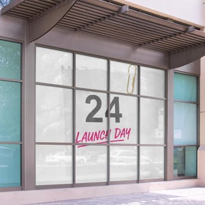 以下が含まれることがあります： 大きな窓のある建物の外観。数字の「24」が表示され、その下に筆記体で「LAUNCH DAY」と書かれています。金色のペーパークリップが窓にぶら下がっています。建物はモダンなデザインです。