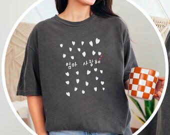 May include: A dark gray t-shirt with a white graphic of hearts and the Korean text "엄마 사랑해" (meaning "Mom I love you").