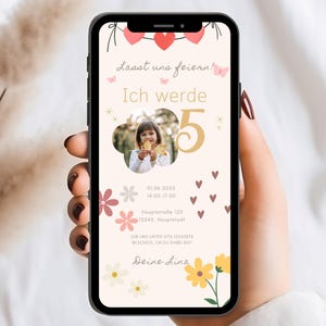 Pode incluir: Um smartphone exibe um convite de aniversário com o texto "Lasst uns feiern! Ich werde 5". O convite apresenta uma foto de uma menina, decorações florais e de coração, e detalhes do evento. O telefone é segurado.