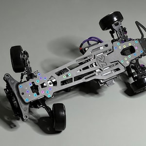 以下が含まれることがあります： リモートコントロールカー用の黒と灰色のカーボンファイバーシャーシ。シャーシは、さまざまな穴と切り抜きを備えた詳細な設計になっています。シャーシには、さまざまなネジとナットが装備されており、その一部は色付けされています。