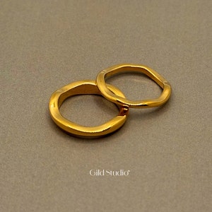Puede incluir: Dos anillos de color dorado, uno ligeramente más grande que el otro, están apilados uno encima del otro. Los anillos son lisos y tienen una forma ligeramente irregular.