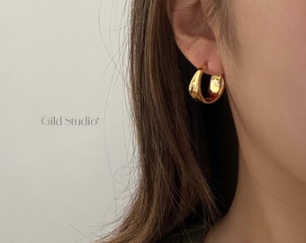 May include: Gold hoop earrings with a textured surface. The earrings are worn in a person's ear.