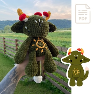 Könnte beinhalten: Grünes Häkeltier aus Plüsch in Form einer Kreatur mit einem Sonnendesign auf der Brust. Das Spielzeug hat rote und gelbe Akzente auf dem Kopf und einen weißen Schwanz.