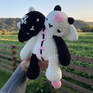 May include: A handmade, two-headed plush toy. One head is black with a white star, the other is white with a pink heart. The toy is stitched together with pink yarn and has black and white limbs.