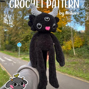 Może przedstawiać: Czarna szydełkowa lalka z trzema oczami, szarymi rogami i różowymi ustami. Lalka ma długie, smukłe kończyny. Tekst "CROCHET PATTERN" i "by Amikoro" są widoczne u góry obrazu. Tło jest rozmyte.