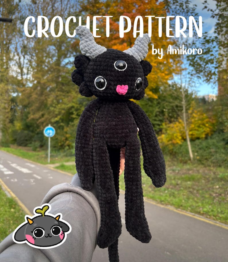 May include: A black crochet plush toy featuring three eyes, two grey horns, and a small pink tongue. The text CROCHET PATTERN by Amikoro is visible at the top, and a small graphic of the creature is located in the bottom left corner.