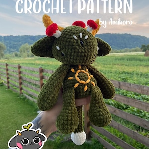 May include: A handmade green crochet doll with yellow and red accents, featuring a sun design on its chest. The doll has horns and mushroom-like details. The text "CROCHET PATTERN by Amikoro" is displayed at the top.
