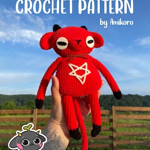 Puede incluir: Muñeca roja de ganchillo con cuernos, ojos y pies negros, y una estrella blanca en el pecho. La muñeca tiene brazos y piernas largos y una cola. El texto "CROCHET PATTERN by Amikoro" está en la parte superior de la imagen.