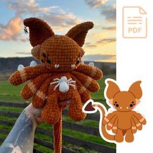 May include: Crochet amigurumi pattern of a brown and orange creature with a long tail and eight legs. The creature has a white spider on its chest. The pattern is available as a PDF download.