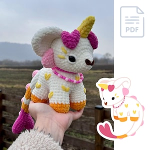 May include: A crocheted amigurumi toy in the shape of a unicorn with a pink and yellow tail and horn. The toy is white with yellow and pink accents and has a pink beaded necklace.