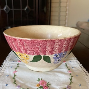May include: A vintage ceramic mixing bowl with a pink, white, and green floral design. The bowl has a slightly textured surface and is in good condition.