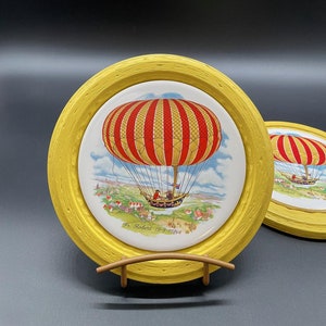 May include: Two yellow framed ceramic plates with a red and yellow hot air balloon illustration. The plates feature the text "Fr. Robert 19-9-1783".