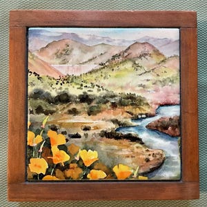 May include: A watercolor painting of a landscape with a river, mountains, and yellow flowers in the foreground. The painting is framed in a wooden frame.