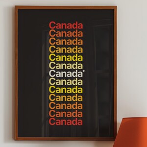 Puede incluir: Una impresión enmarcada con la palabra "Canadá" repetida en un degradado de rojo, naranja y amarillo sobre un fondo negro. Un tocadiscos de estilo vintage y una lámpara con una pantalla naranja están sobre una superficie de madera.