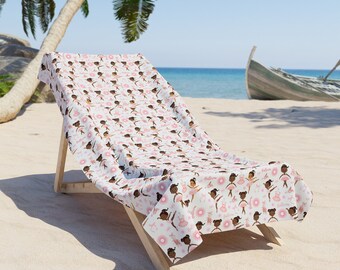 Könnte beinhalten: Ein weißer Strandstuhl mit einem gemusterten Strandtuch. Das Handtuch zeigt ein sich wiederholendes Muster aus braungebrannten Ballerinas, die rosa Tutus und rosa Blumen tragen. Der Stuhl steht auf einem Sandstrand mit einem Holzboot im Hintergrund.
