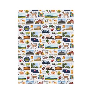Op de afbeelding: Witte stof met een herhaald patroon van illustraties met het thema Nebraska. Het ontwerp bevat afbeeldingen van herten, bezienswaardigheden, eten en stadsnamen zoals Omaha, Lincoln en Kearney. Het algemene thema is een viering van Nebraska.