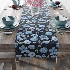 May include: A blue and white floral table runner with a dark blue background. The runner is made of fabric and has a repeating pattern of flowers and leaves.