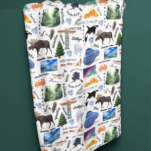 May include: A white fabric with a repeating pattern of Alaskan landmarks, animals, and cities. The pattern includes a moose, a bear, a whale, a fish, a mountain range, a forest, a totem pole, and the words "Fairbanks", "Ketchikan", "Whittier", "Wasilla", "Sitka", "Anchorage", "Knik-Fairview", "Arctic Ocean", "Pacific Ocean", and "Seward".