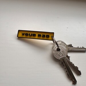 May include: A yellow keychain with the text "YOUR R36" in black lettering. The keychain has a silver key ring with three keys attached.