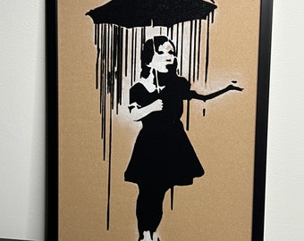 May include: A black and white stencil art print of a girl holding an umbrella in the rain. The print is on a brown background and is signed "Banksy" in the bottom right corner.