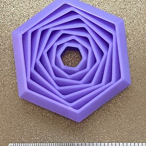 May include: Purple plastic hexagon cookie cutter with five concentric rings. The cutter is about 1 inch in diameter.