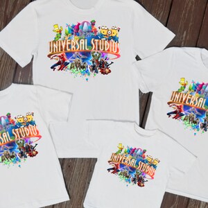 Może przedstawiać: Cztery białe koszulki z kolorowym nadrukiem graficznym przedstawiającym różne postacie z kreskówek i tekstem "Universal Studios".