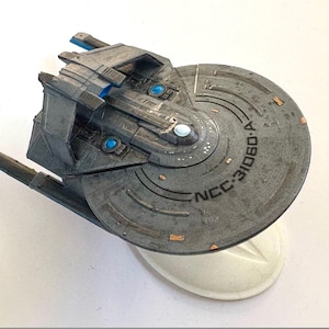 Puede incluir: Maqueta gris de una nave espacial con un casco circular con el texto "NCC-31080-A". El modelo tiene detalles azules y cobrizos y est&aacute; montado sobre un soporte blanco. Un art&iacute;culo de colecci&oacute;n.