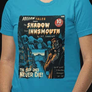 Könnte beinhalten: Ein türkisfarbenes T-Shirt mit einem Vintage-Comic-Cover-Design, das eine schattenhafte Figur und den Text "ARKHAM TALES The Shadow Over Innsmouth by H.P. Lovecraft THE DEEP ONES NEVER DIE!" zeigt.