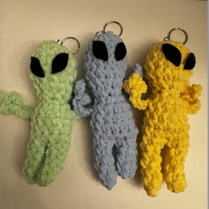 May include: Three handmade alien keychains in green, blue, and yellow. Each plush alien has large black eyes and a silver keyring. The aliens have outstretched arms and are made of a soft, textured yarn.
