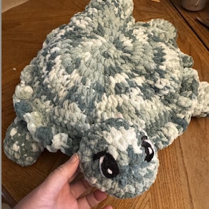 May include: A crocheted plush turtle toy in shades of green and white. The turtle has black eyes and a soft, fuzzy texture.