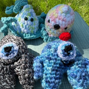 May include: Four crocheted octopus plushies in different colors and patterns. The plushies have large eyes and are made with a soft, textured yarn.